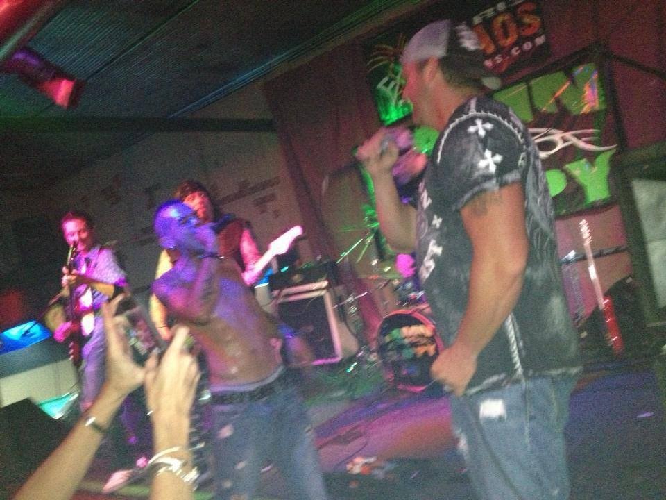 Band performing live with crowd in front, colorful neon stage lighting