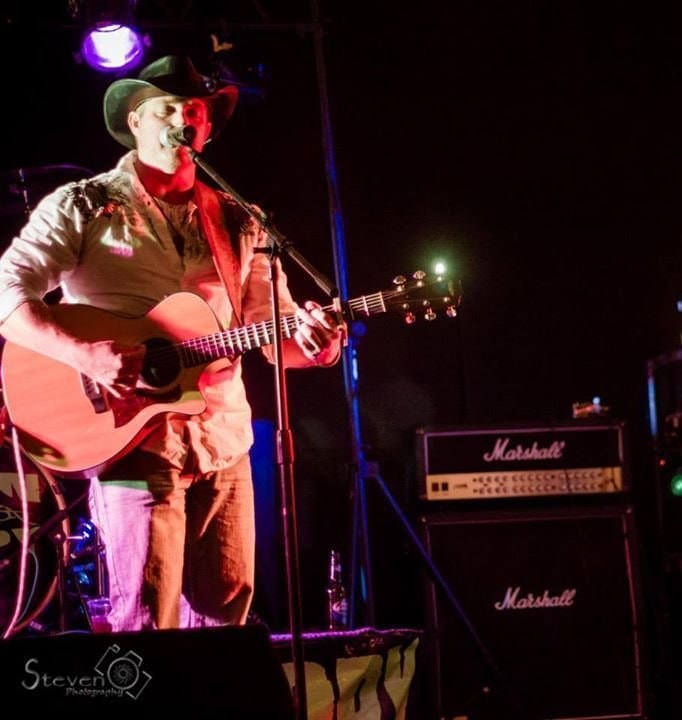 Marc Kenney performing with acoustic guitar on stage, Marshall amp behind him