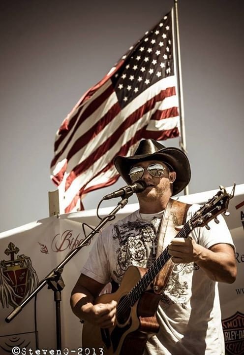 Marc Kenney performing outdoors at a Harley-Davidson event with American flag backdrop