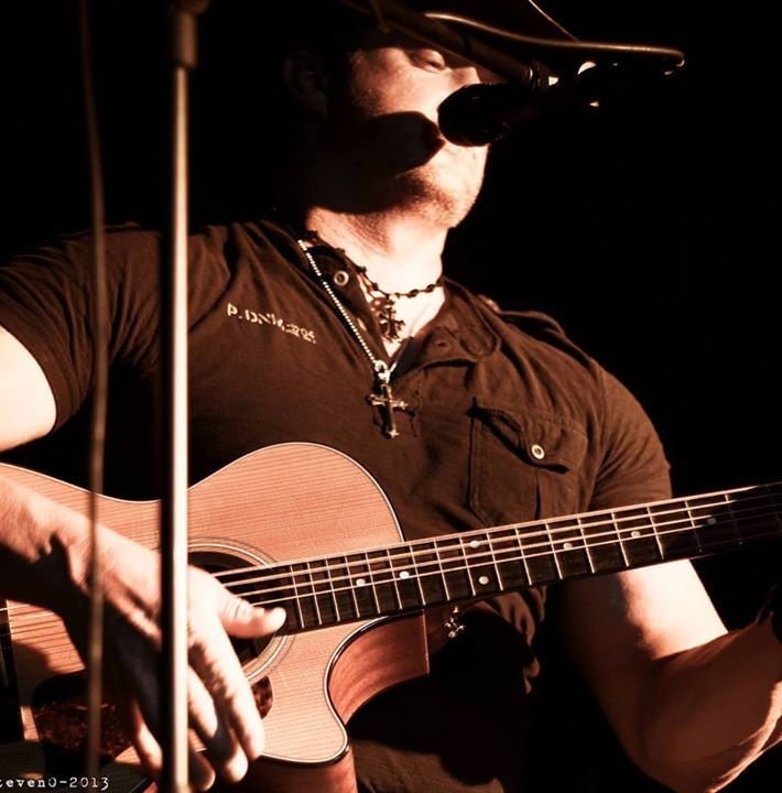 Marc Kenney with acoustic guitar by a creek, sepia tone